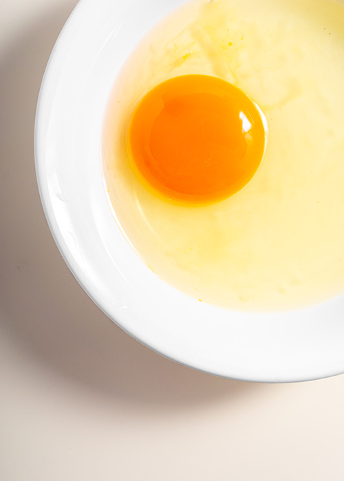 Raw egg with deep orage yolk, in a white bowl